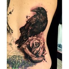 a woman's stomach with a black bird and rose tattoo on the side,