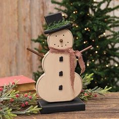 a wooden snowman sitting on top of a table next to a christmas tree and books