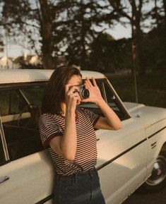 a woman standing next to a white car while holding a camera up to her face