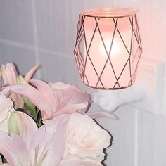 a vase with pink flowers and a lit candle on the wall next to some lights