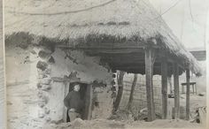 an old black and white photo of a man in front of a hut