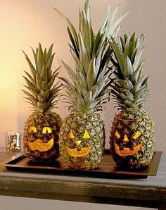 three pineapples with jack - o'- lanterns carved into them on a tray