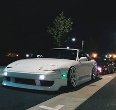 two white cars parked next to each other on the side of a road at night