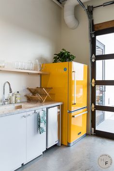 a yellow refrigerator sitting in the middle of a kitchen next to a sink and cabinets