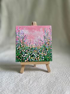 a small easel with a painting on it sitting on a white cloth covered surface