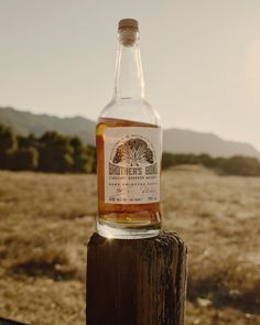 a bottle of whiskey sitting on top of a wooden post in the middle of a field