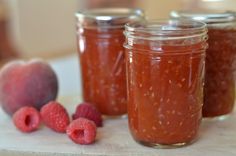 three jars filled with raspberry jam next to fresh raspberries on a cutting board