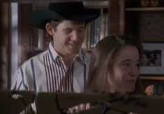 a man and woman sitting next to each other in front of a bookshelf