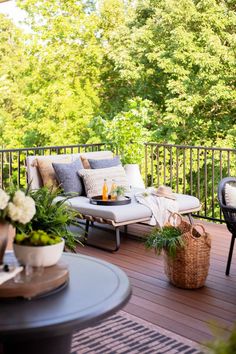 a patio with chairs, tables and plants on the outside deck overlooking trees in the background