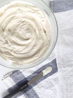 a glass bowl filled with cream sitting on top of a checkered towel next to a knife