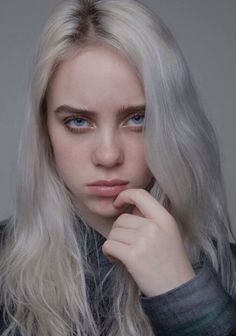 a woman with long blonde hair and blue eyes posing for a photo in front of a gray background