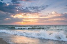 the sun is setting over the ocean with waves crashing on the beach and clouds in the sky