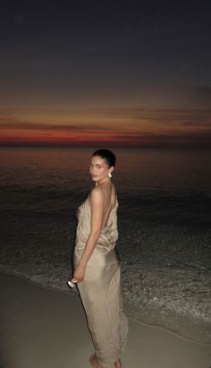 a woman standing on top of a sandy beach next to the ocean at night time