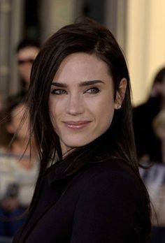 a woman with long brown hair and blue eyes smiling at the camera while standing in front of a crowd