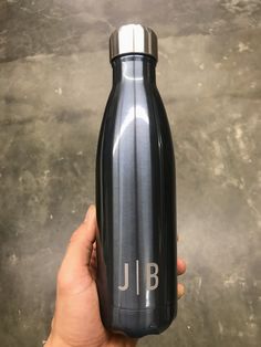 a person holding up a black and silver water bottle with the word j b on it