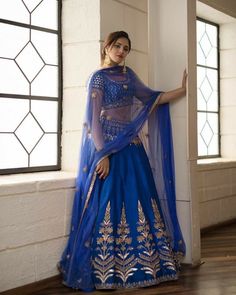 a woman in a blue and gold lehenga standing by a window with her arms on the wall