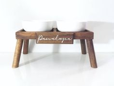 two white bowls sitting on top of a wooden stand with the word panelope written in cursive writing