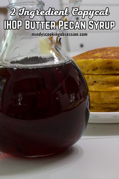 a glass pitcher filled with liquid next to pancakes on a plate and text overlay reads 2 ingredient copycat hop butter pecan syrup