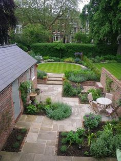 an outdoor garden with lots of green plants and flowers in the center, surrounded by brick buildings