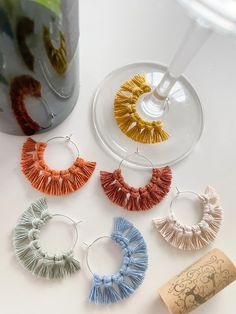 four pairs of tasseled hoop earrings sitting next to a wine glass