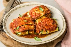 a white plate topped with lasagna covered in sauce and garnished with green leaves