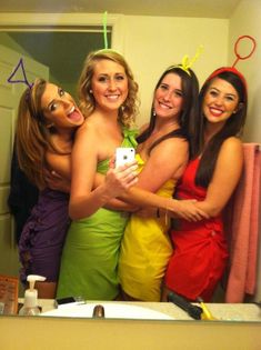 three women in dresses taking a selfie in front of a bathroom mirror with one holding a cell phone