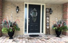 two large planters with plants are on the front steps of a brick house, next to a black door