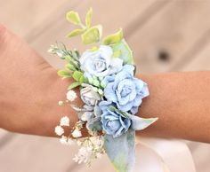 a wrist corsage with blue flowers and greenery on it's arm