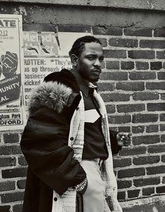 a black and white photo of a man standing in front of a brick wall wearing a coat