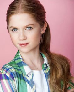 a woman with long red hair wearing a green and white shirt posing for a photo