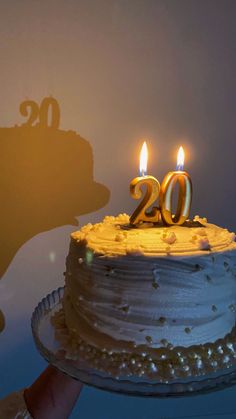 a person holding a cake with candles in the shape of 20 and twenty on it