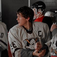 a hockey player is talking to his team in the dugout with other players behind him