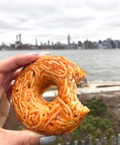 a person holding up a doughnut with spaghetti on it in front of a body of water