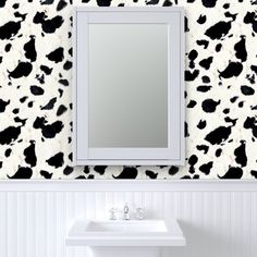 a white sink sitting under a mirror next to a black and white cow print wall