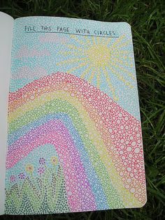 a notebook covered in lots of different colored dots and rainbows on the cover is laying on some green grass