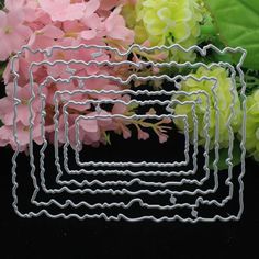 four pieces of metal wire sitting next to some pink and green flowers on a black surface