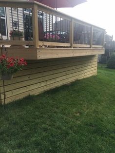 a wooden deck with flower boxes and an umbrella over it on the grass in front of a house