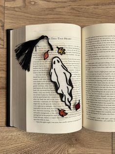 an open book on a wooden table with a paper cut out of a ghost