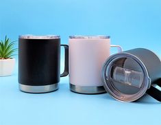 three different types of coffee mugs on a blue surface with a plant in the background