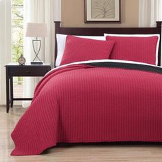 a bed with red bedspread and pillows on top of it in a room