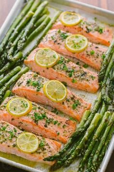 salmon and asparagus on a baking sheet with lemons, parsley and seasoning