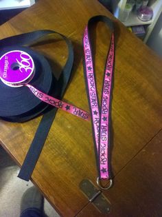 a purple lanyard with pink and black letters on it sitting on top of a wooden table