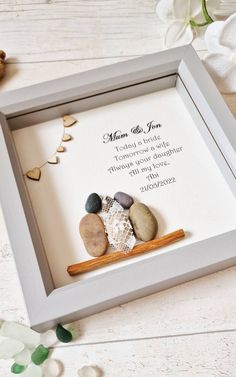 a white frame with some rocks and a wooden stick in it on top of a table