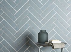 a gray vase sitting on top of a table next to a white tiled wallpaper