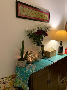 a table with flowers and candles on it in front of a wall mounted art piece