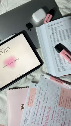 an open laptop computer sitting on top of a bed next to a book and pen