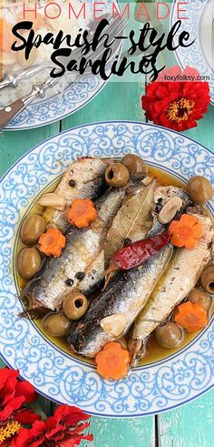 some fish and olives are on a blue and white plate next to red flowers