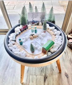 a toy train set on top of a table with snow and trees in the middle