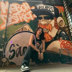 a woman sitting on the ground in front of a wall with graffiti