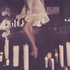 a woman in a white dress is standing next to candles with her legs spread out